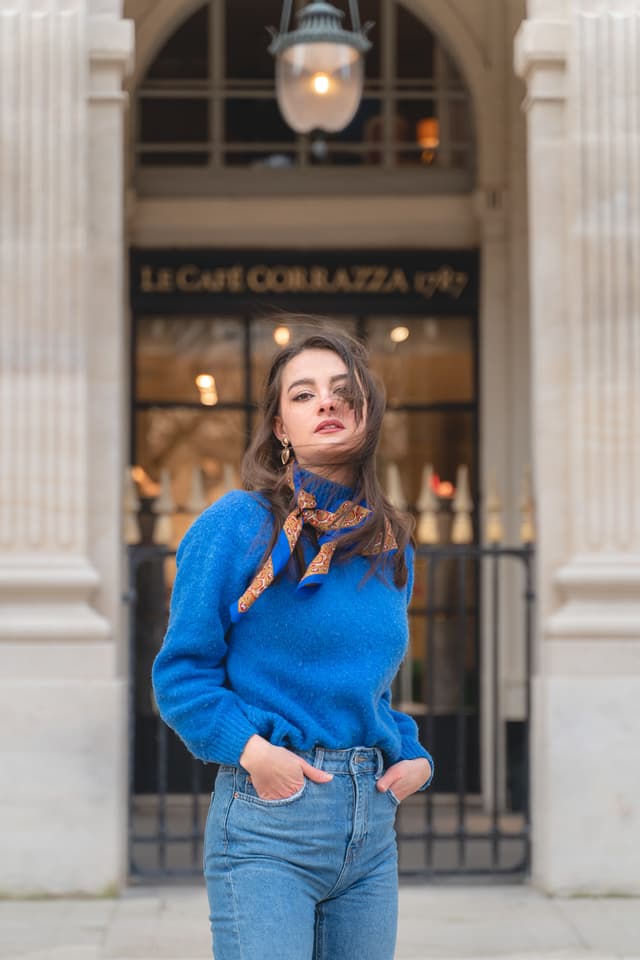 Portrait of a womanwearing a blue sweater outside a classic Parisian cafe during a Paris photoshoot.