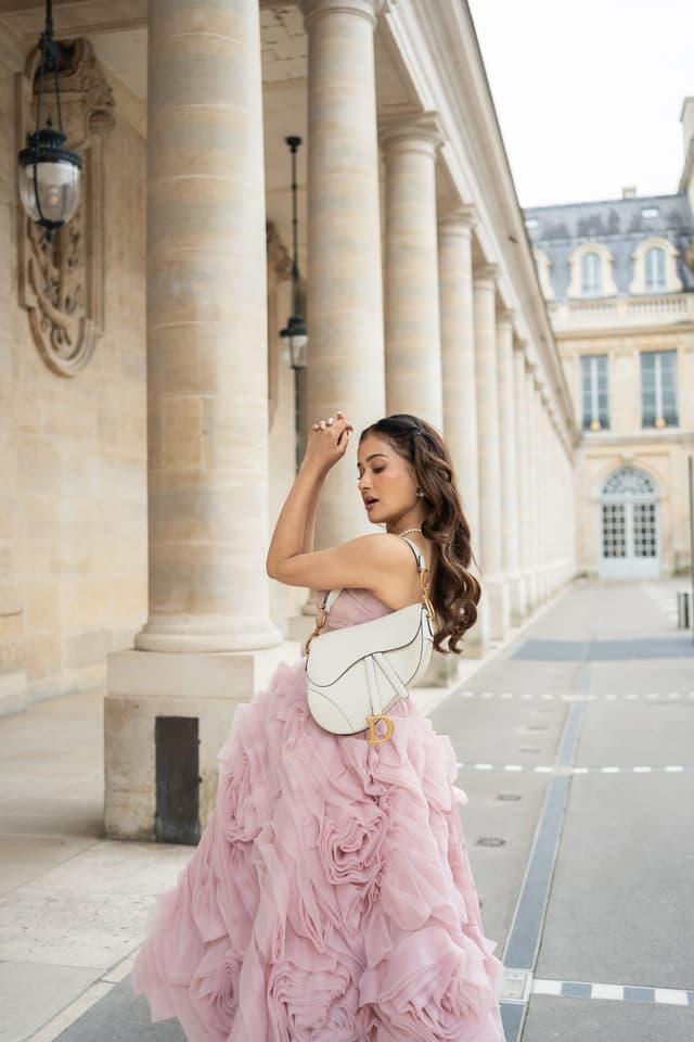 Woman in a pink dress posing between the historic stone columns of Palais Royal for a portrait photo session in Paris.