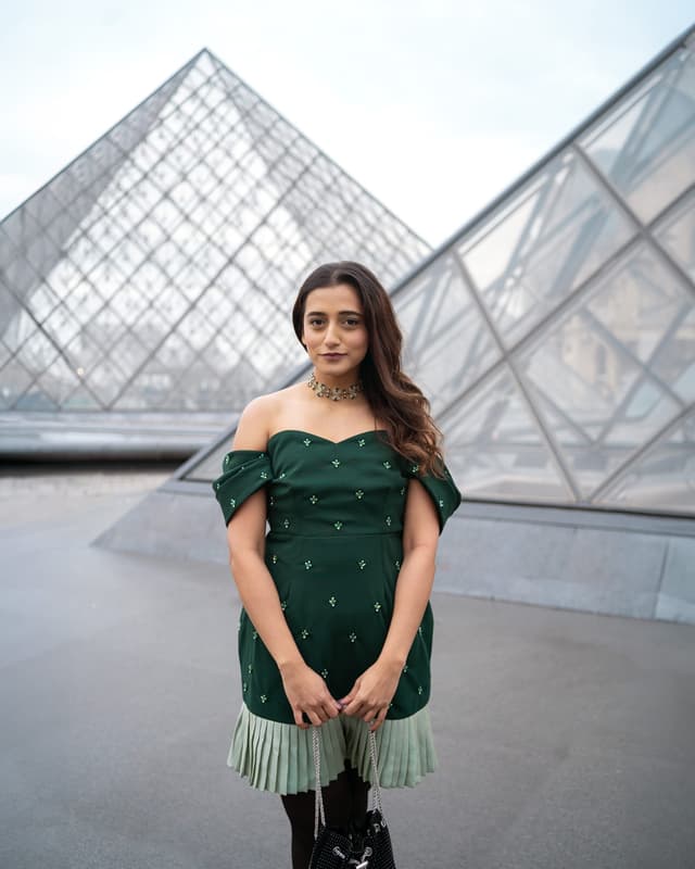 woman posing directly in front of the glass Louvre Pyramid during a private portrait photo session in Paris.