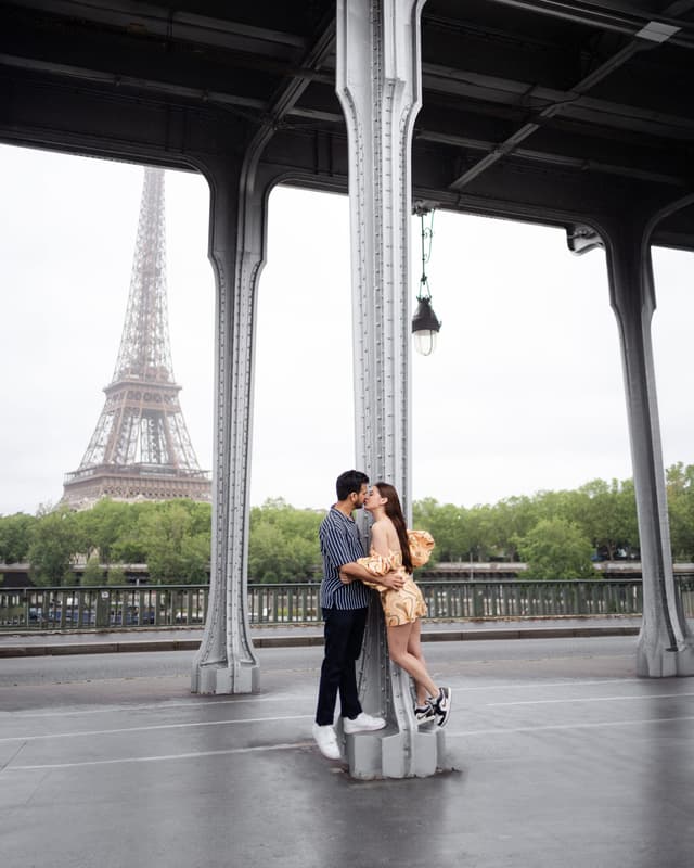 Couple standing together under the steel pillars of Bir-Hakeim Bridge during an Eiffel Tower photo session in Paris.
