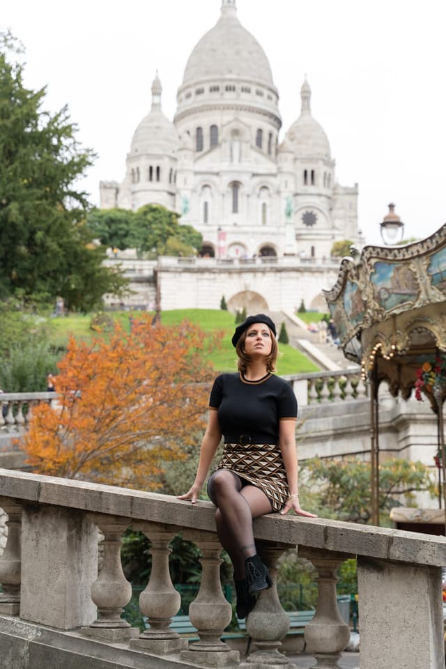 Woman sitting on a stone ledge in Montmartre with Sacré-Cœur Basilica in the background during an vintage photo session in Paris.