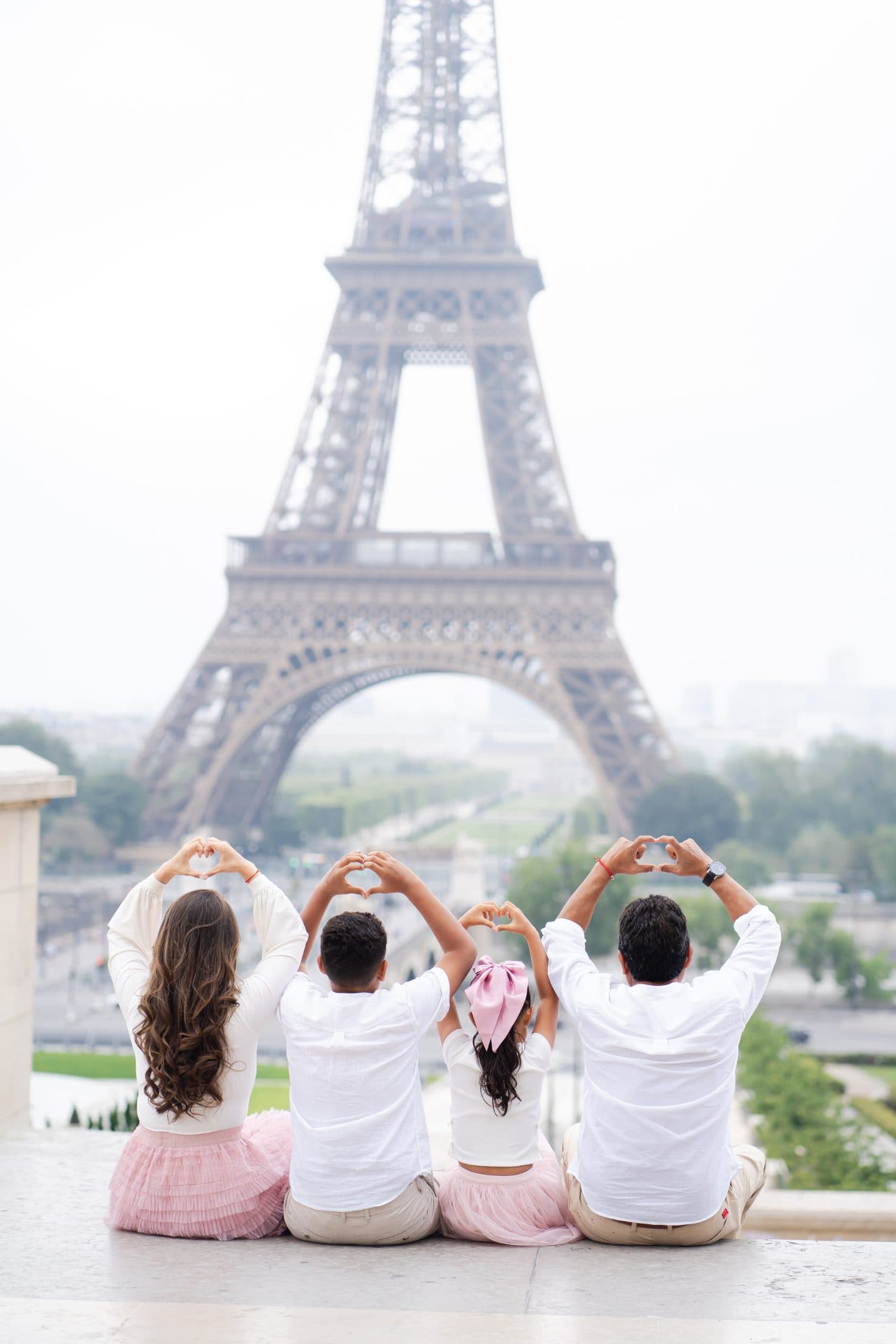 ack view of a family forming heart shapes with their hands during an Eiffel Tower photo session in Paris.