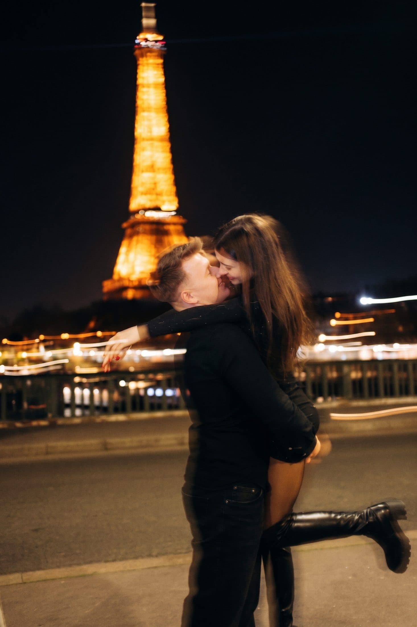 Man lifting his partner at night in front of the illuminated Eiffel Tower during a romantic Paris photoshoot.