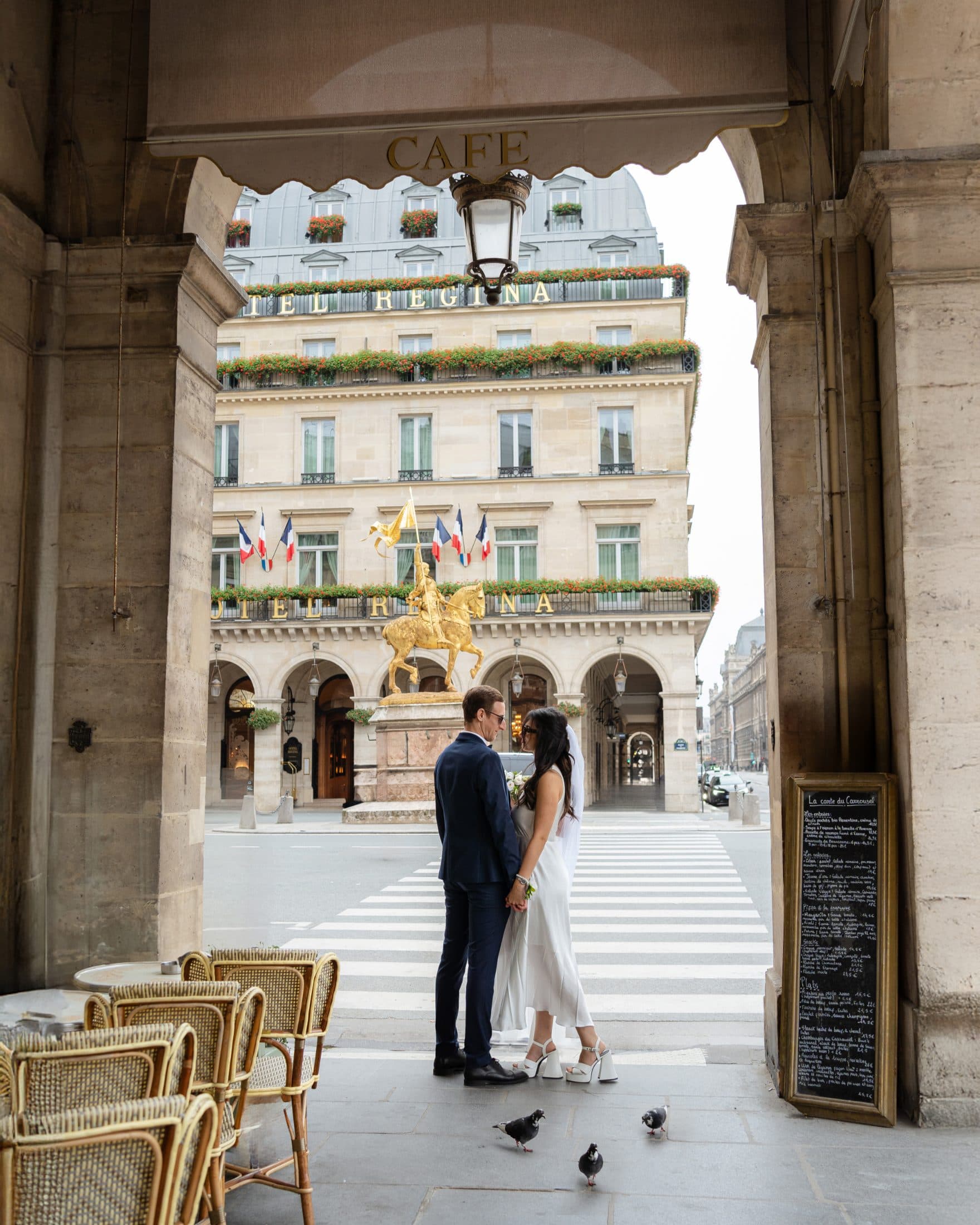 Elopement couple embracing under a classic Paris café arcade near Place des Pyramides.